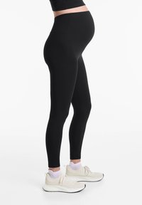 Fekete kismama leggings, magas derékkal és sima, rugalmas anyagból. Világos színű sportcipőkkel és bokazoknival párosítva.