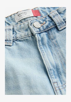 Lyseblå mid-rise denimjeans med knaplukning og kontrastsyning. Etiketten siger "BARREL MID RISE, MADE IN BANGLADESH."