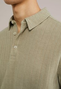 Polo shirt in soft, textured green fabric with a ribbed pattern, featuring a classic collar and three button placket.