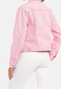 Rosa denimjacka med en kortad design, kontrasterande sömmar och knappdetaljer vid ärmsluten och nederkant, sedd bakifrån.
