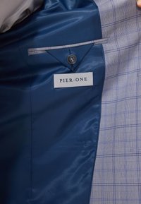 Blå og grå rutet dressjakke innside med blå satengforing, en knapp og et vevd merke som leser "PIER·ONE."