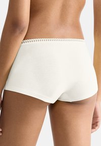Pantaloni corti crema a vita media con una texture morbida, dotati di un grazioso bordo in pizzo lungo la vita. Tessuto liscio e vestibilità su misura.