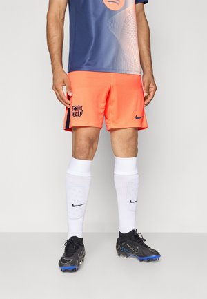 Nike Barcelona football shorts in bright orange with navy accents, featuring the team logo. Paired with white socks and black football cleats.