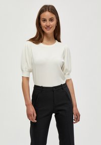 Vit stickad topp med korta puffärm, rund halsringning, matchad med mörka byxor som har knapp och sidofickor. Slät textur.