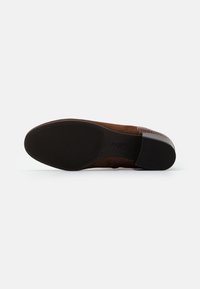Zapato de ante marrón con un respaldo texturizado de patrón de cocodrilo, suela de goma negra contrastante y bordes suaves. La parte inferior presenta detalles de agarre.