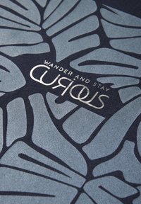 Textil med ett blått och mörknavy bladmönster; har silverfärgad text som säger "WANDER AND STAY" och "CURIOUS." Slät textur.