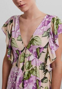 Robe florale avec un décolleté en V, des manches courtes volantes et un détail de bouton, ornée de fleurs roses et violettes sur un fond beige.