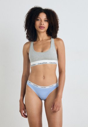 Grå sportsbh med Calvin Klein-logo i livet; lyseblå bikini-bunn med matchende logo-stripe. Stoffet ser glatt og elastisk ut.