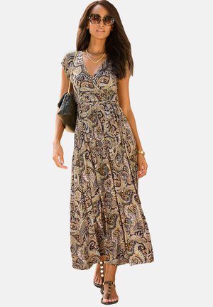 Frau trägt ein Maxikleid mit Paisley-Muster, schwarze Sandalen mit goldenen Akzenten, große Sonnenbrille, geschichtete goldene Halsketten, eine Uhr und trägt eine schwarze Handtasche.