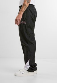 Pantalons de survêtement noirs en tissu léger, dotés d'une taille élastique, d'une broderie rouge sur le côté et d'accents blancs contrastants au bas.