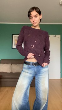 Maglione color marrone con fori visibili e lavorazione a maglia strutturata, abbinato a jeans a gamba larga celesti con motivo sbiadito. Cintura nera a contrasto.