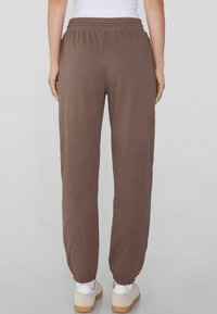 Braune Sweatpants mit einem gerafften Taillenbund, elastischen Bündchen und einer lockeren Passform. Sie haben eine glatte Textur und minimalistische Details.