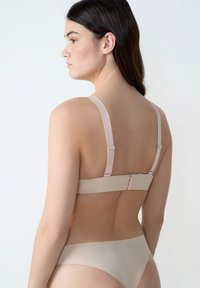 Soutien-gorge beige avec bretelles réglables et fermeture à crochets au dos, présentant une texture lisse et un design minimaliste.