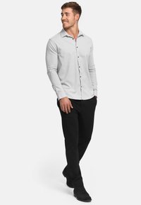 Lichtgrijs overhemd met lange mouwen en knopen met een kraag, zwarte knopen, gecombineerd met zwarte broek en zwarte schoenen, wat een contrasterende outfit oplevert.