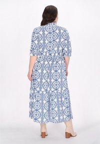 Rochie lungă cu un fundal alb și modele circulare albastre, manșete trei sferturi și talie ajustată. Asortată cu cizme cu toc bej deschis.