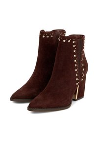 Botas de ante burdeos por el tobillo con puntera afilada, acentos de tachuelas doradas a lo largo de los lados y un tacón metálico grueso. Textura suave, líneas limpias.