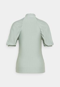 Haut vert clair à manches courtes bouffantes, col haut, et détail de tissu froncé le long des coutures des épaules, vu de dos.