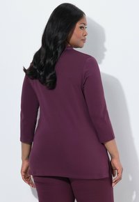 Lila Langarmshirt mit geradem Schnitt, seitlichen Schlitzen und glatter Textur. Mit rundem Ausschnitt und kombiniert mit einer passenden Hose.
