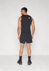 Svart ermela treningsgenser og svarte shorts, med logoen plassert på baksiden. Materialet ser lett og pustende ut, designet for bevegelse.