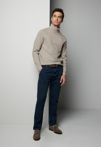 Beige stickad polotröja med strukturerat mönster, marinbl�å byxor, brun läderbälte och grå loafers. Enfärgad bakgrund.
