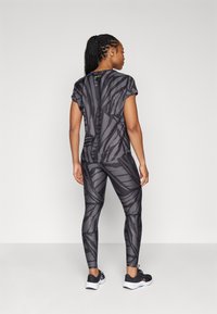 Tettsittende atletisk antrekk i svart med grå tigerstripe-mønster. Korte ermer, fukttransporterende stoff, kombinert med matchende leggins og joggesko.