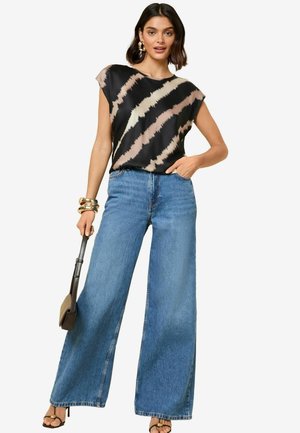 Sort og tan-farvet top med et takkete mønster, parret med brede blå denimjeans. Tilbehøret inkluderer en taske og armringe.