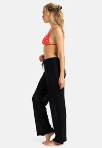 Rood en oranje gestreepte driehoek bikini-top gecombineerd met losse, zwarte netbroek met een trekkoord in de taille en uitgesneden chevronpatronen.