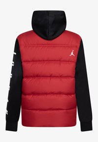 Rød polstret jakke med sort hætte og ærmer, med ribbede manchetter og et hvidt logo på venstre side. Glat tekstur, quiltet design.