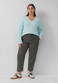Hellblaues, grobstrickiges Sweater mit V-Ausschnitt, kombiniert mit dunkelgrauen Jogginghosen und beigen Sneakers mit schwarzen Akzenten.