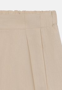 Beige linnen rok met een elastische taille, voorzien van een geplooid ontwerp en een gestructureerd oppervlak. De stof lijkt lichtgewicht en ademend te zijn.