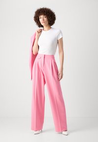 High-waisted pink trousers with wide legs, a smooth texture, and front pleats, paired with a fitted white t-shirt and a light pink blazer.