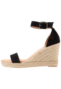 Sandalo con tacco a cuneo in suede nero con cinturino alla caviglia, caratterizzato da una suola in juta intrecciata e un design di cinturini minimalista. Texture liscia con punta rotonda.