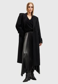Black wool trench coat over a black fuzzy sweater, paired with a metallic pleated skirt and knee-high black heeled boots.