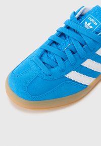 Sapatilha atlética azul com parte superior em camurça, design de três riscas brancas e língua texturizada; apresenta uma sola de borracha de goma e atacadores planos.