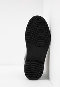 Semelle de chaussure en caoutchouc noir avec un motif de semelle texturé, présentant des détails en relief et un bord lisse. Construction robuste et profil plat.