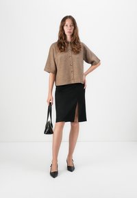 Brun, kortermet strikket cardigan med knapper, kombinert med et svart skjørt med høyslitt, og svarte spisse hæler.