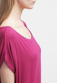 Loose-fitting, short-sleeved top in bright pink fabric with a wide neckline and soft texture, draping comfortably over the body.