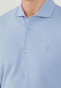 Polo shirt di un azul chiaro realizzato in tessuto testurizzato, con colletto classico, tre bottoni e un piccolo logo ricamato sul petto.