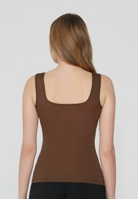 Top de tirantes marrón, ajustado, con escote cuadrado, tirantes anchos y una textura suave. El dobladillo es limpio, sin costuras visibles.