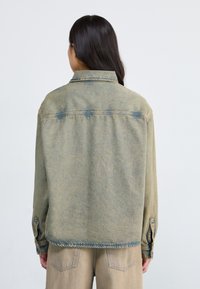 Faded green denim jacket with a collared neck, buttoned cuffs, and a straight cut. Features light distressing and contrasting stitching details.