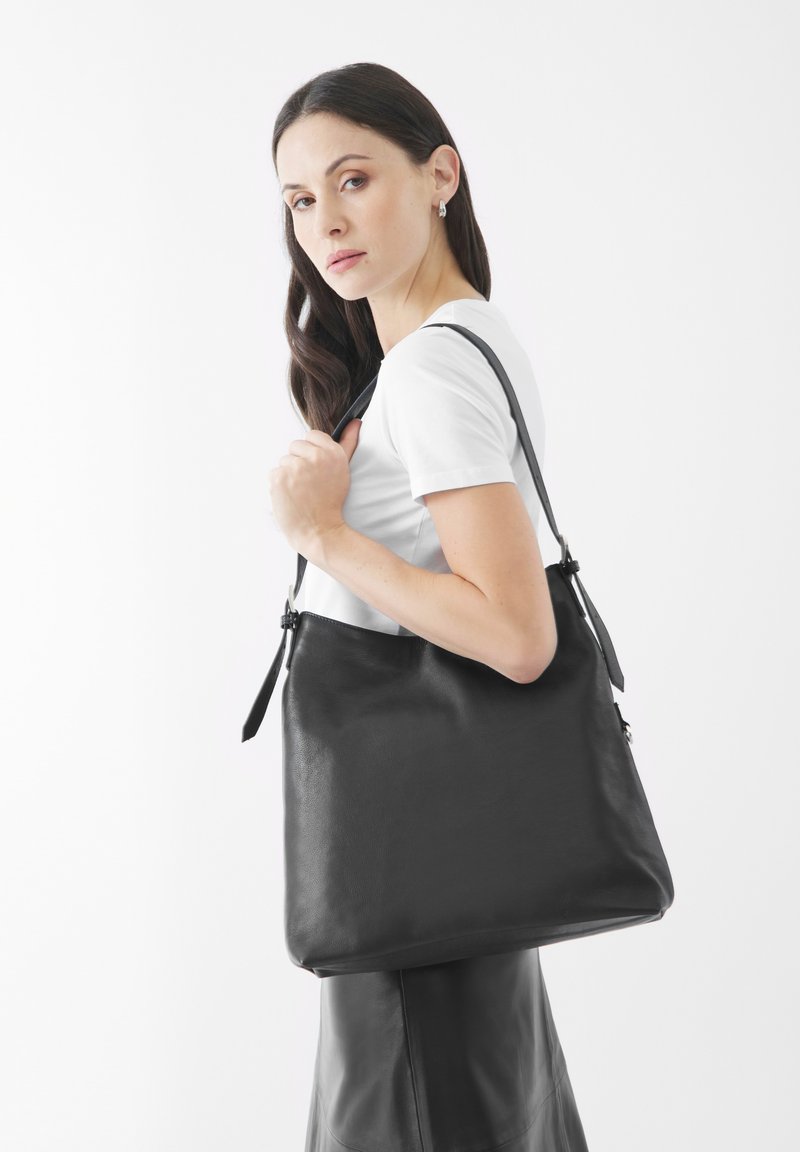 Zwarte leren tote bag met een gladde textuur, voorzien van een enkele verstelbare schouderband en een subtiele vouw aan de bovenkant.