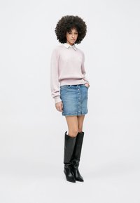 Svetloružový rebrovaný sveter s bielym golierom, v kombinácii s džínsovou sukňou so zapínaním na predné gombíky a čiernymi čižmami po kolená.