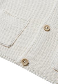 Cárdigan de punto color crema con tejido texturizado, dos bolsillos frontales tipo parche y botones de madera.