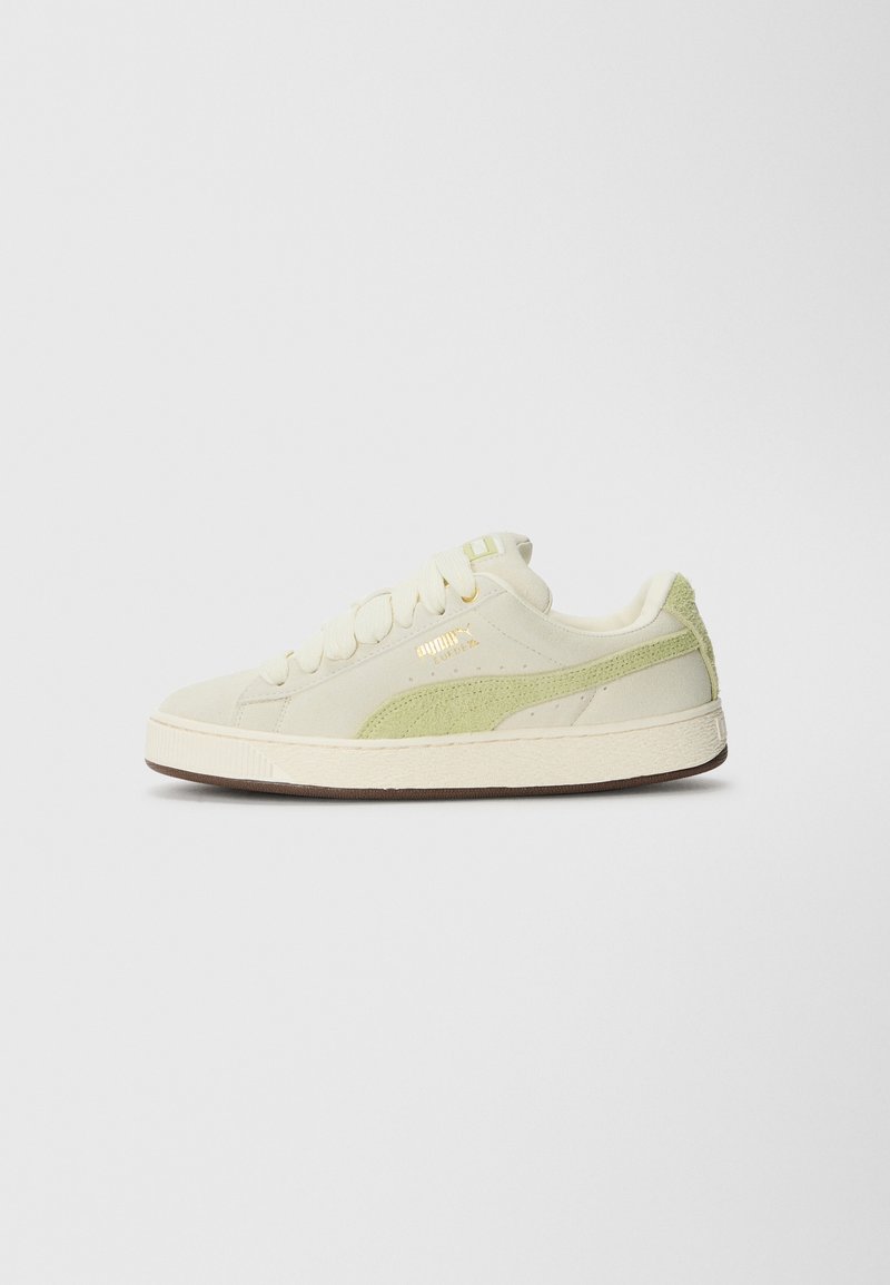 Niedrig geschnittene Puma Suede Sneaker in Off-White mit einem hellgrünen Wildlederstreifen und goldenem Logo an der Seite, cremefarbenen Schnürsenkeln und brauner Sohle.