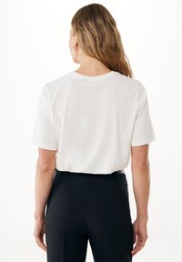 Bílé tričko s krátkým rukávem, volný střih, s kulatým výstřihem. Nosené s černými kalhotami s vysokým pasem, které ukazují jednoduchý, čistý design.