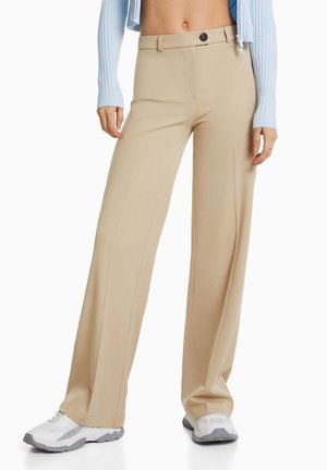 Beige levelet hameet, joissa on sileä rakenne, nappikiinnitys ja vyölenkit. Yhdistetty tiukkaan vaaleansiniiseen toppiin ja valkoisiin lenkkikenkiin.