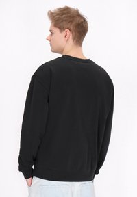 Zwarte sweatshirt met lange mouwen, ribgebreide boorden en zoom, ronde hals, gemaakt van zacht materiaal, met een relaxte pasvorm en een minimalistisch ontwerp.