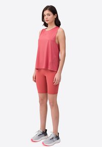 Top atlético sin mangas de color rosa combinado con pantalones cortos de ciclismo a juego y zapatillas de correr grises con acentos rosas, con un corte relajado y una textura suave.