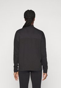 Sort sweatshirt med en tekstureret bagpanel, ribbede manchetter og krave. Bæres med matchende sorte leggings.