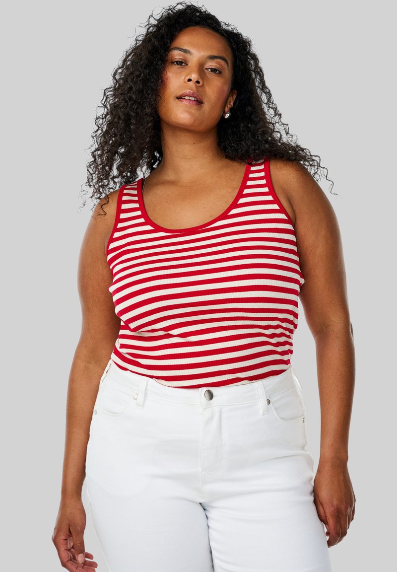 Top con rayas rojas y blancas, de textura acanalada y tirantes anchos, combinado con jeans blancos de cintura alta.